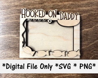 May include: A wooden picture frame with the text "HOOKED ON DADDY" at the top. The frame has a fishing rod and fish cutouts. The frame is blank and ready for a photo.
