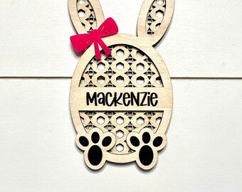 May include: Wooden Easter bunny cutout with a pink bow and the name Mackenzie. The bunny is decorated with a geometric pattern and has paw prints at the bottom.