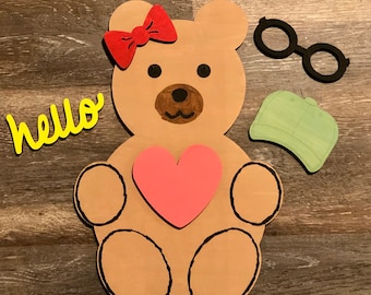 May include: A brown felt teddy bear with a red bow, a pink heart, and the word "hello" in yellow felt. The bear is holding the heart in its paws.
