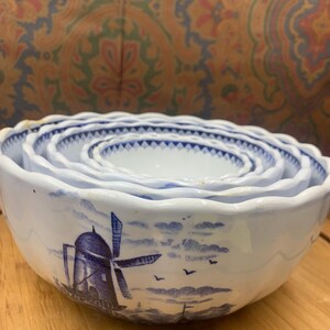 May include: Set of four white ceramic mixing bowls with a blue windmill and landscape design. The bowls nest inside each other. The rims have a scalloped edge and a blue patterned border.