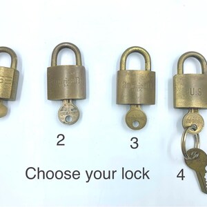 May include: Four brass padlocks labeled 1, 2, 3, and 4, each with a key inserted. The locks feature the text American U.S. or U.S. engraved on the front. The text Choose your lock is printed at the bottom. Each padlock has a rounded shackle.