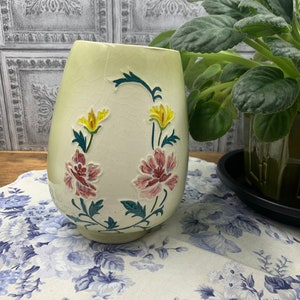 May include: A pale green ceramic vase with a floral design. The vase has a crackled glaze and features pink and yellow flowers with green leaves.