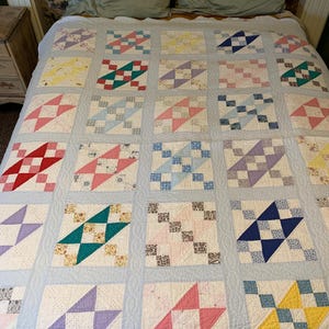 May include: A patchwork quilt featuring a light blue background with a grid of square blocks. Each block contains a star-shaped pattern in various colors including red, pink, yellow, purple, blue, and green, combined with floral and checkered fabric prints.