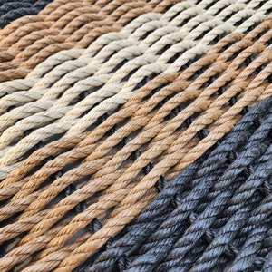 May include: A close-up of a woven rope hammock with black, brown, and beige ropes. The ropes are woven together in a diagonal pattern.