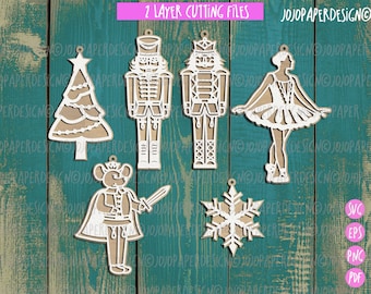 May include: A set of five laser cut Christmas ornaments featuring a nutcracker, a ballerina, a Christmas tree, a snowflake, and a mouse. The ornaments are white and are designed to be layered for a 3D effect.