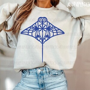 K&ouml;nnte beinhalten: Ein hellgraues Sweatshirt mit einem blauen Mandala-artigen Mantarochen-Design. Das Sweatshirt wird von einer Person mit langen braunen Haaren getragen.