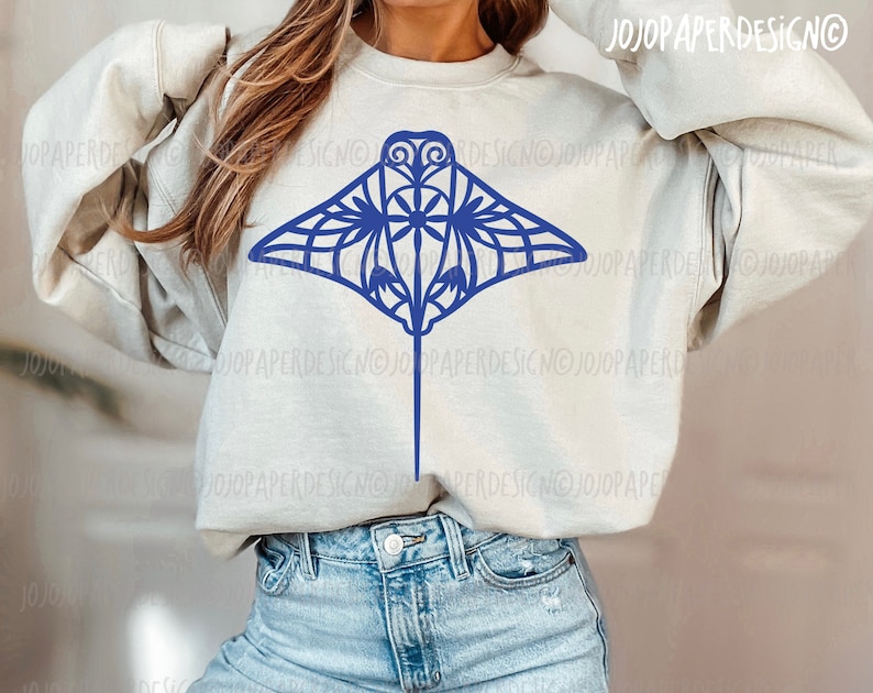 K&ouml;nnte beinhalten: Ein hellgraues Sweatshirt mit einem blauen Mandala-artigen Mantarochen-Design. Das Sweatshirt wird von einer Person mit langen braunen Haaren getragen.
