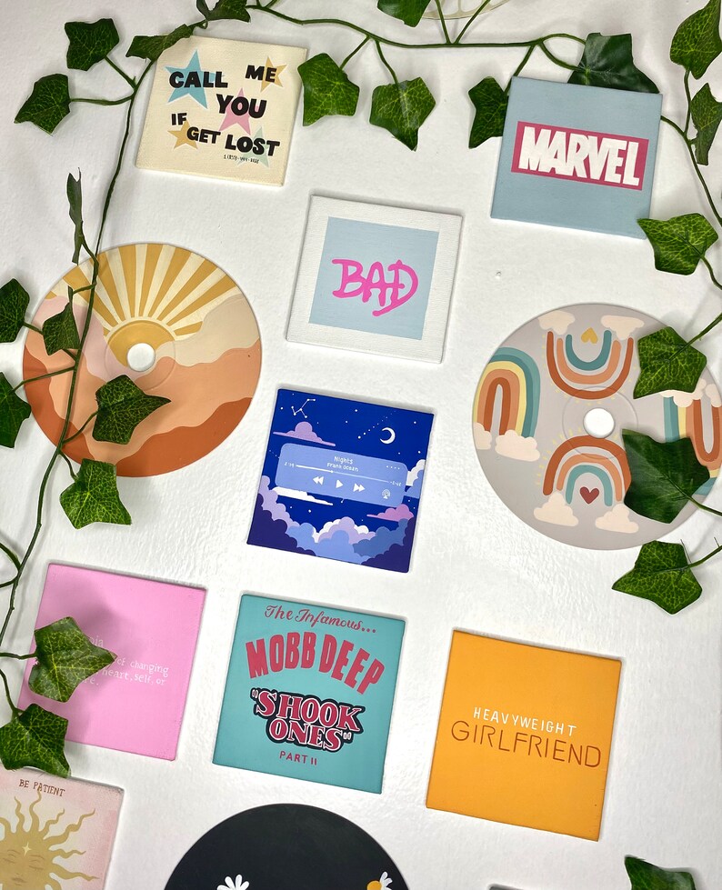 K&ouml;nnte beinhalten: Eine Sammlung quadratischer und runder dekorativer Magnete mit verschiedenen Designs und Texten. Die Magnete zeigen S&auml;tze wie "CALL ME IF YOU GET LOST" und "HEAVYWEIGHT GIRLFRIEND", zusammen mit einem "MARVEL"-Logo und Albumcovern.