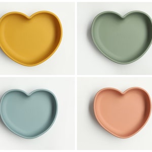 May include: Four heart-shaped silicone plates in yellow, green, blue, and pink. The plates are designed for babies and toddlers.