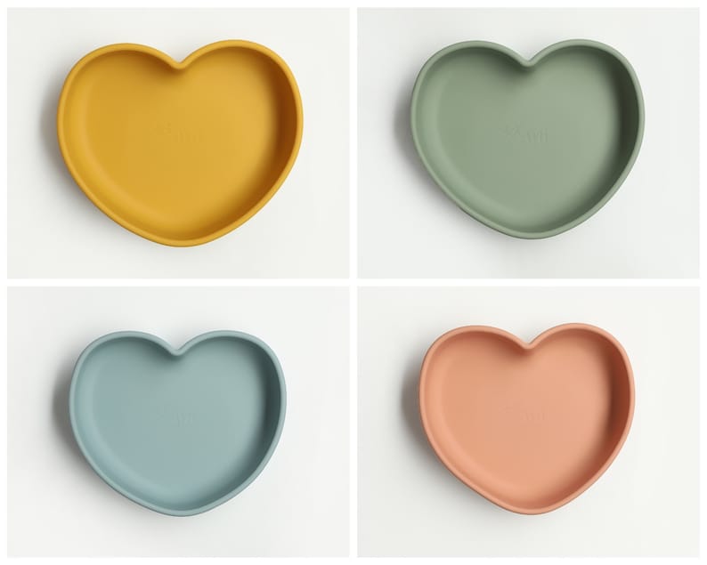May include: Four heart-shaped silicone plates in yellow, green, blue, and pink. The plates are designed for babies and toddlers.