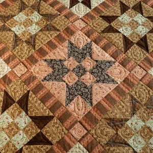 May include: A quilt in shades of brown, beige and peach. The quilt is made up of a variety of different patterns, including stars, squares and stripes. The quilt is quilted with a decorative stitch.