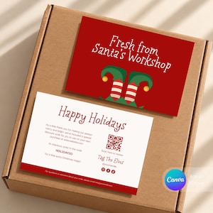 May include: A brown cardboard box containing two rectangular cards. The top card is red with white text reading Fresh from Santa's Workshop and a graphic of elf shoes. The bottom card is white with red text reading Happy Holidays.