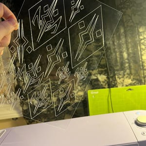 Op de afbeelding: Een doorzichtig plastic vel met een herhalend geometrisch patroon van vierkanten en driehoeken. Het patroon is in het plastic ge&euml;tst.