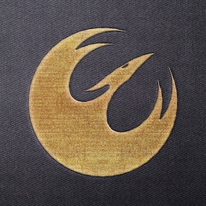 Op de afbeelding: Een goudkleurig Rebel Alliance-symbool, ook bekend als het Phoenix Squadron-symbool, op een donkerblauwe stoffen achtergrond.