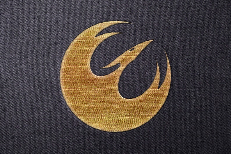 Op de afbeelding: Een goudkleurig Rebel Alliance-symbool, ook bekend als het Phoenix Squadron-symbool, op een donkerblauwe stoffen achtergrond.