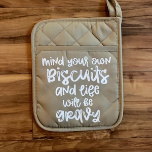 May include: Beige quilted oven mitt with the text "Mind your own biscuits and life will be gravy" in white.