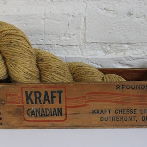 May include: A wooden box with the text "Kraft Canadian" and "Kraft Cheese Limited Outremont, Que." printed on it. The box contains a ball of yellow yarn. The box is labelled "2 pounds net."