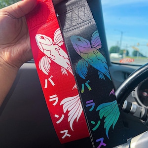 May include: Two black and red car keychains with a white and iridescent fish design. The keychains have Japanese text that reads "パ ラ ン ス".