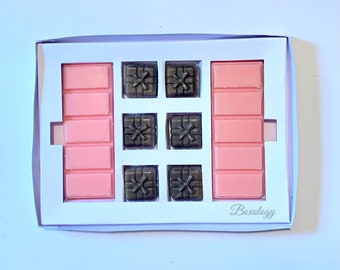May include: A white box with a pink and brown wax melt set. The box has the text "Boxology" printed on the bottom right corner. The wax melts are arranged in a grid pattern with six brown gift box shaped melts and two pink rectangular melts.
