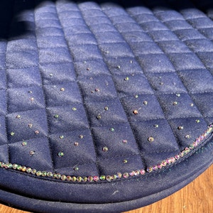May include: A navy blue saddle pad with a quilted design and a row of iridescent rhinestones around the edge.