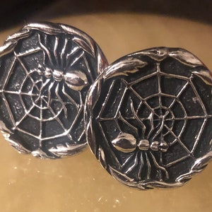 May include: A pair of silver cufflinks featuring a spider in a web design.