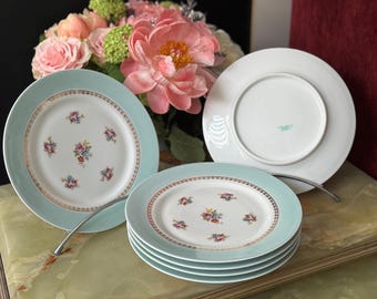 May include: Set of four white ceramic plates with a light blue rim and a floral pattern. The plates are stacked on top of each other.