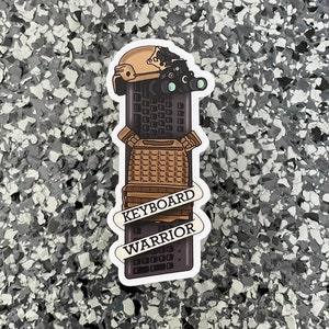 May include: A sticker featuring a keyboard design with military gear, including a helmet and night vision goggles. The text "KEYBOARD WARRIOR" is displayed on a banner across the keyboard.