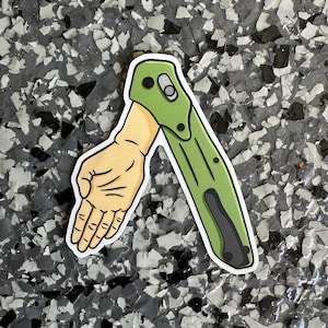 May include: A green and black pocket knife sticker with a cartoon hand reaching out. The sticker is on a gray and white speckled surface.