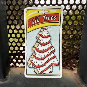 May include: A white and red Christmas tree-shaped air freshener with the text "Lil' Trees" on a yellow background.