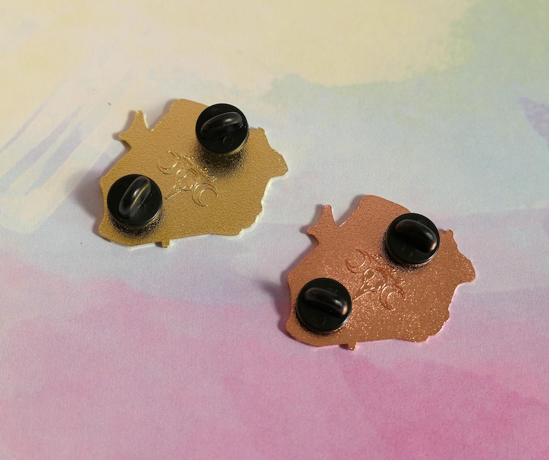 May include: Two gold-colored metal pins with black backs. The pins are shaped like a stylized mountain range. The pins have a black metal pin back.