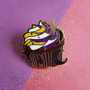 Peut inclure: Une épingle en métal doré en forme de cupcake avec un glaçage violet, blanc et jaune. Le glaçage a un motif en spirale et de petites étoiles.