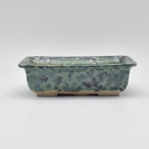 Könnte beinhalten: Ein rechteckiger grüner Keramik-Bonsai-Topf mit einer marmorierten Glasur und vier kleinen Füßen.