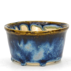 Peut inclure: Un bol en céramique fait à la main avec un glaçage unique. Le bol présente un extérieur bleu foncé qui se fond dans des tons bleu clair et crème. Il possède un bord marron et de petits pieds, mettant en valeur un mélange d'art et de fonctionnalité.
