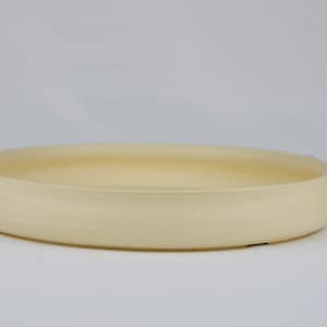 Op de afbeelding: Een grote, gebroken witte keramische serveerschaal met een afgeronde rand. De schaal staat op een wit oppervlak.