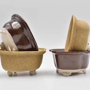 May include: Two brown and beige ceramic bonsai pots with a textured finish. The pots have a rounded shape and three small feet. The pots are stacked on top of each other.