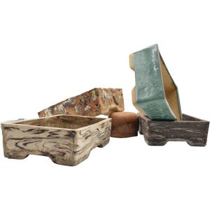 Könnte beinhalten: Vier Keramik-Bonsai-Töpfe in verschiedenen Farben und Stilen. Die Töpfe sind rechteckig und haben eine strukturierte Oberfläche. Ein Topf ist hellbraun mit einer Holzmaserung, ein anderer ist dunkelbraun mit einer Holzmaserung, ein weiterer ist hellgrün mit einer glatten Oberfläche und der letzte ist hellbraun mit einer rauen Oberfläche.