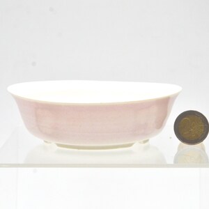 Peut inclure: Un bol en céramique peu profond et rond avec un extérieur rose pâle et un intérieur blanc. Le bol présente une petite base surélevée et est placé à côté d'une pièce de deux euros pour l'échelle, mesurant 25,75 millimètres de diamètre.