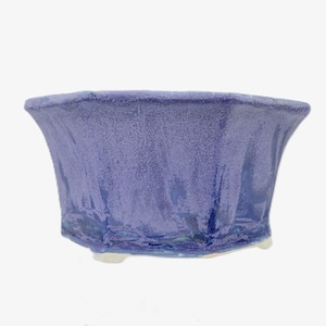 Könnte beinhalten: Eine handgefertigte Keramikschale mit einem ausgestellten, strukturierten Design. Die Schale ist ein gedämpftes Periwinkle-Blau mit einem gesprenkelten Finish und einem dunkelblauen Sockel. Die Schale steht auf einem weißen Sockel.