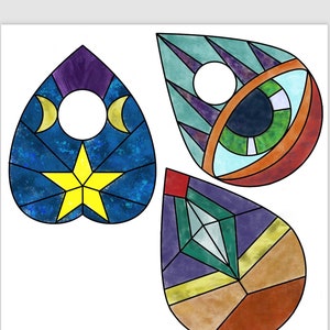 May include: Three stained glass style ornaments in the shape of teardrops. The first ornament is a blue heart with a yellow star and two crescent moons. The second ornament is a teal and purple teardrop with a large eye in the centre. The third ornament is a purple, green, and brown teardrop with a diamond shape in the centre.