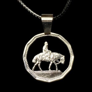 Può includere: Collana con pendente in argento raffigurante una scena equestre dettagliata. Il pendente mostra un cavaliere a cavallo all'interno di una cornice circolare, sospeso a una catena d'argento. Il design presenta un cavaliere e un cavallo su sfondo nero.