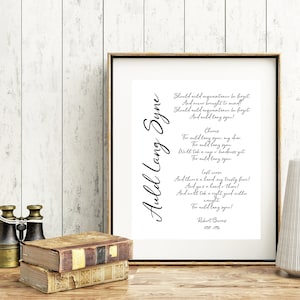 Puede incluir: Una impresión de arte imprimible en blanco y negro con la letra de la canción "Auld Lang Syne" de Robert Burns. La letra está escrita en cursiva y está centrada en la página. El título de la canción está escrito en una fuente más grande y se encuentra en la parte superior de la página.