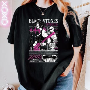 K&ouml;nnte beinhalten: Schwarzes T-Shirt mit einer Manga-Illustration einer S&auml;ngerin, die eine rosa Gitarre spielt, mit dem Text "BLACK STONES" und japanischen Schriftzeichen. Das Shirt enth&auml;lt auch den Text "WANA OSAKI GAIA RECORDS".