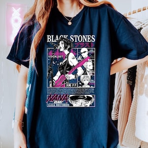 K&ouml;nnte beinhalten: Marineblaues T-Shirt mit einem Manga-Grafikdesign der Band "Black Stones". Das Design umfasst japanischen Text, eine S&auml;ngerin mit einer rosa Gitarre und weitere Bandmitglieder im Comic-Stil.