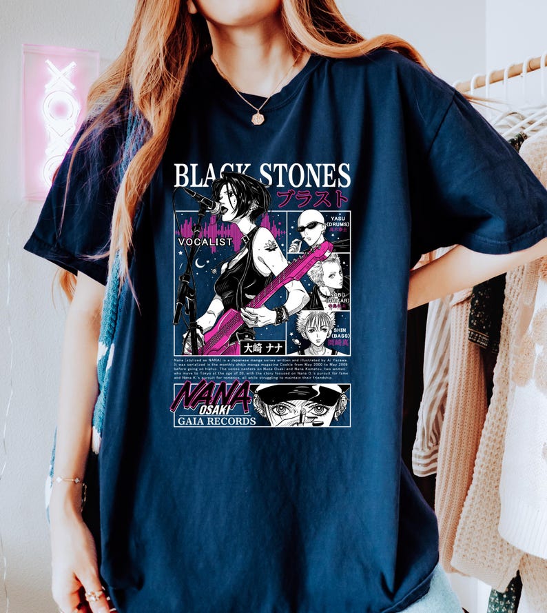 K&ouml;nnte beinhalten: Marineblaues T-Shirt mit einem Manga-Grafikdesign der Band "Black Stones". Das Design umfasst japanischen Text, eine S&auml;ngerin mit einer rosa Gitarre und weitere Bandmitglieder im Comic-Stil.