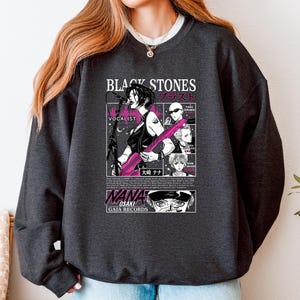 K&ouml;nnte beinhalten: Dunkelgraues Sweatshirt mit einer Manga-Illustration einer S&auml;ngerin, die eine rosa Gitarre spielt. Das Design enth&auml;lt den Text "BLACK STONES" und japanischen Text sowie "NANA OSAKI" und "GAIA RECORDS".