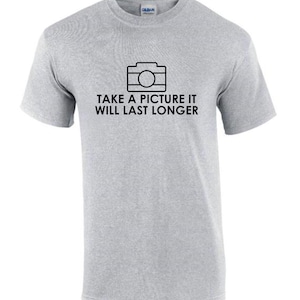 Puede incluir: Camiseta gris claro con un gráfico negro de una cámara y el texto "TAKE A PICTURE IT WILL LAST LONGER". La camiseta es de material suave y tiene mangas cortas.