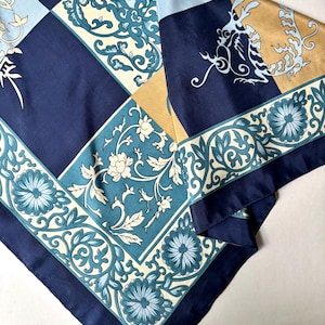 Peut inclure: Un foulard carré présentant un motif à carreaux composé de panneaux bleu marine, bleu clair et dorés. Le design comprend des illustrations complexes d'un dragon, des motifs floraux stylisés et des volutes en blanc et bleu sarcelle.