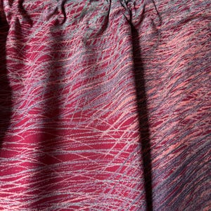 May include: Close-up of a fabric with a red base and a pattern of white and gray lines. The fabric is gathered at the top, creating soft folds. The overall effect is a textured, abstract design.