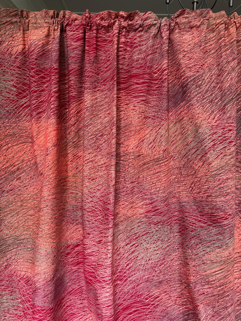 May include: A set of curtains with a vibrant, abstract design. The fabric features a blend of pink, red, and gray hues, with a pattern of fine, wavy lines. The curtains are gathered at the top, creating soft folds.