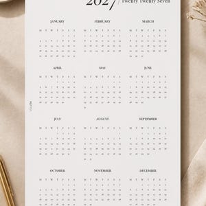 May include: A white paper wall calendar for the year 2027, titled 2027 Twenty Twenty Seven. The calendar displays all twelve months from January to December in a grid format with black text on a white background, including the text BLP CO.
